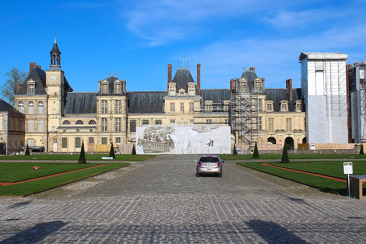 The Cour du Cheval Blanc at Fontainebleau: the wide gravel courtyard with the brick-and-stone wings of the château on a sunny day.
