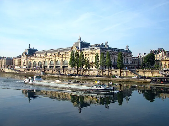 The Musée d'Orsay on the left bank of the Seine, with a barge on the water and its reflection in the river on a clear morning.
