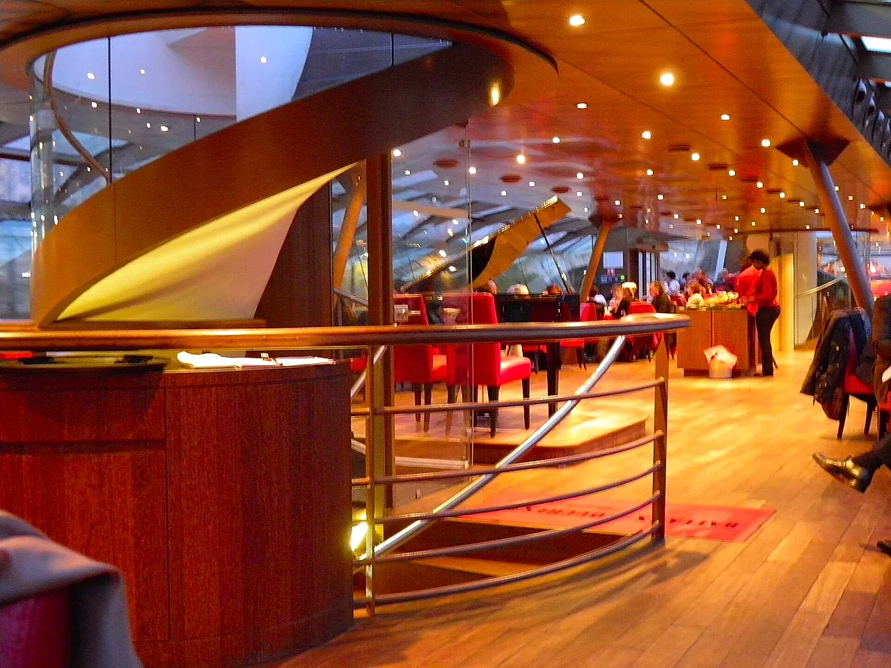 The glazed lower deck of a Seine sightseeing boat, with wood panelling, a railing and passengers at the tables.